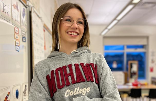 Jessica standing in a kindergarten classroom wearing a Mohawk College hoodie