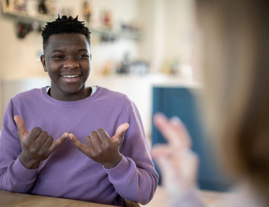 A man in a purple sweater communicating with someone in sign language