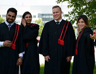 2 male and 2 female graduates in robes outside on campus