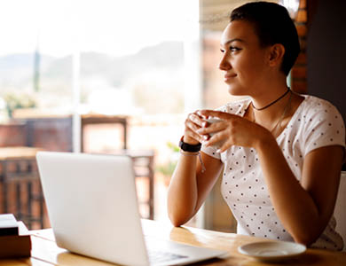 "a female sitting at her computer drinking from a mug"