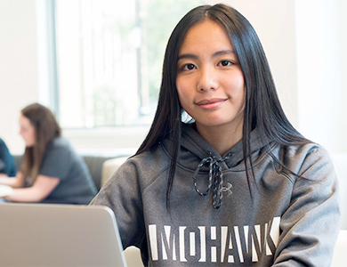 Mohawk student smiling and working on a laptop