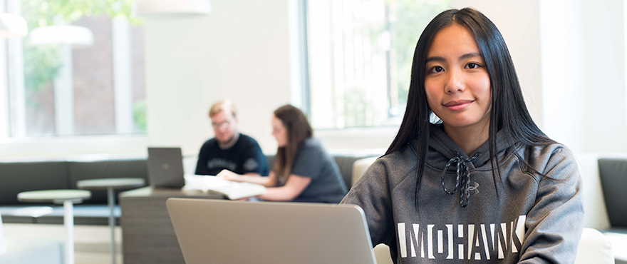 a female working on the computer with a Mohawk hoodie on