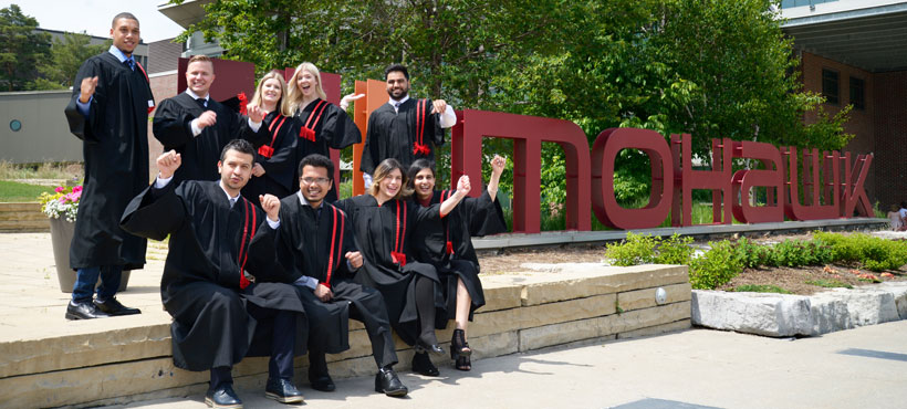 Graduates celebrating infornt of the Mohawk sign