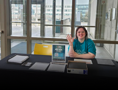 Student working at a booth and waving to the camera