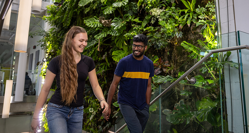 Two students walking in front of the living wall.
