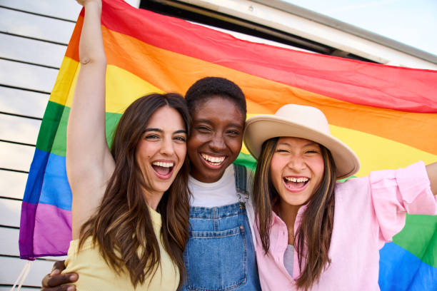 Several smiling young students of varying ethnicities gathered under a pride flag.