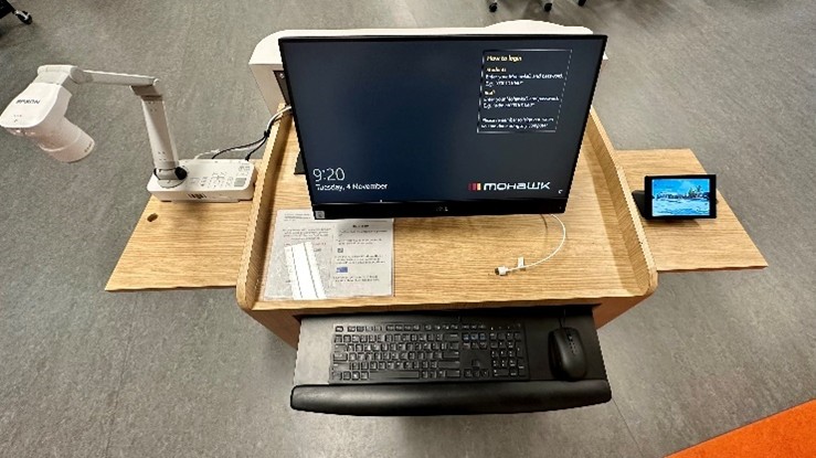 Photo showing a fully equipped Presentation room podium with document camera (left) all-in-one workstation (centre) and room control panel (right)