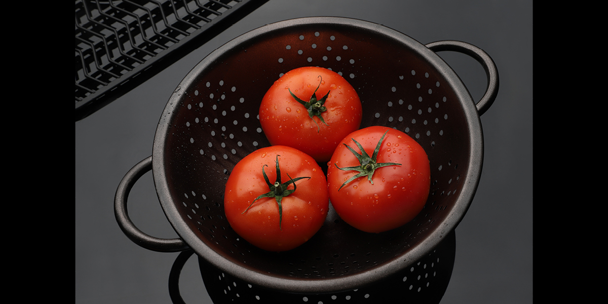 Three wet tomatoes sitting in a colander