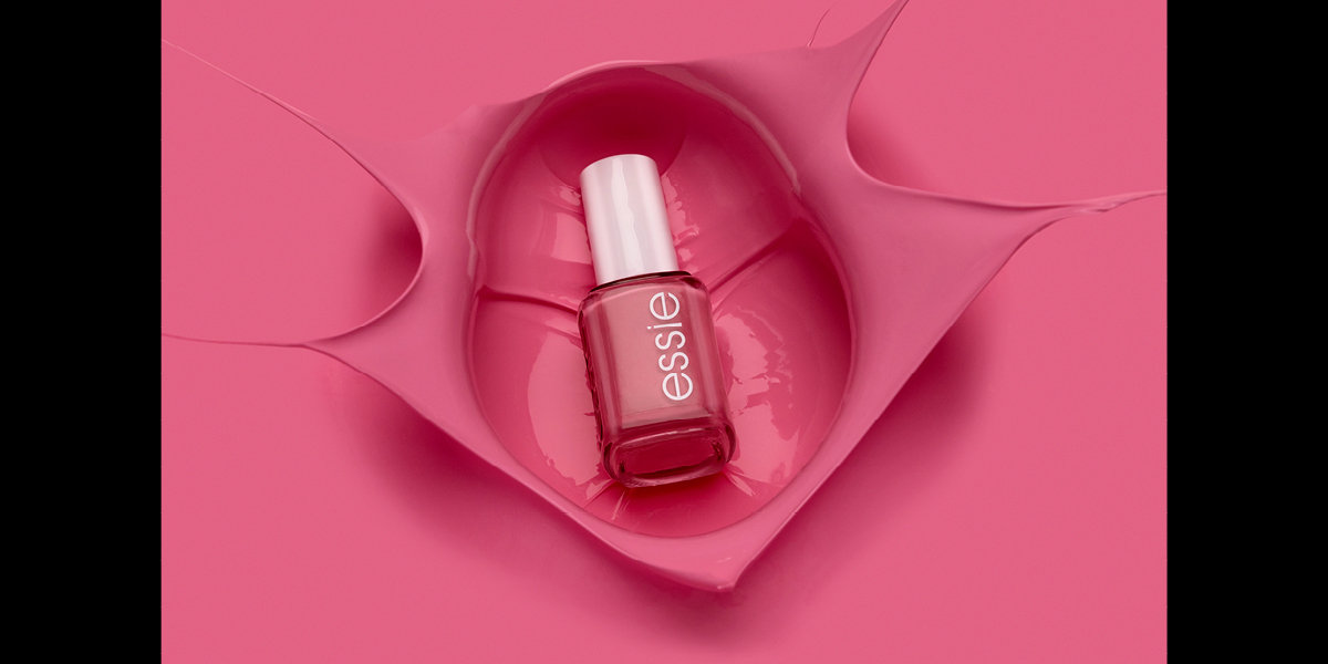 A bottle of pink nail polish landing in a pool of pink nail polish
