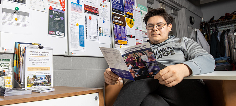 Mohawk College student sitting and reading an Indigenous Education flyer