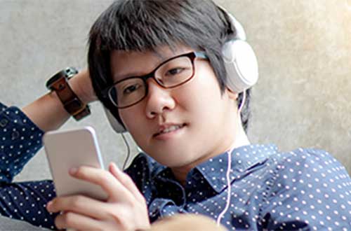 Student with headphones on looking at his phone
