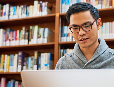 student is reading their laptop in front of lot of books