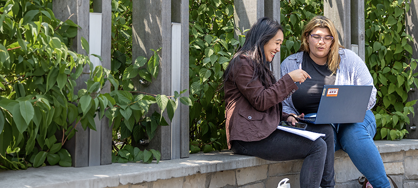 Two Mohawk College students sitting outside and looking at a laptop