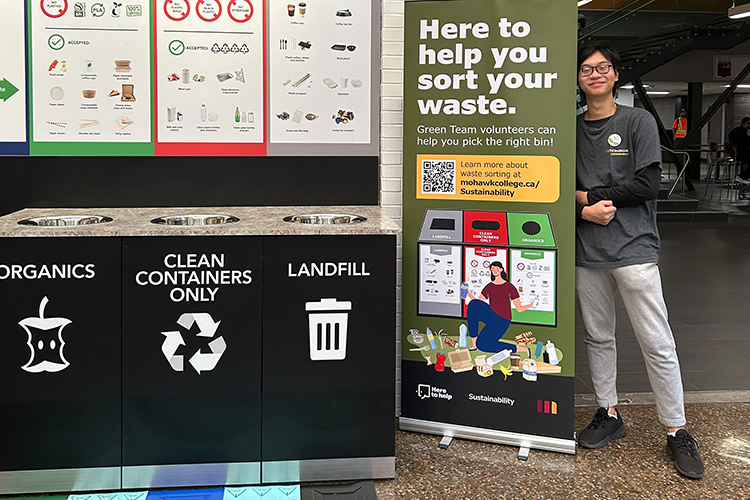 Mohawk college student smiling and posing beside a sustainability banner.