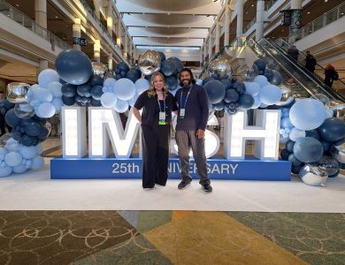 Jess (on left) and Lucky (on right) standing in front of the 'IMSH' sign decorated with balloons