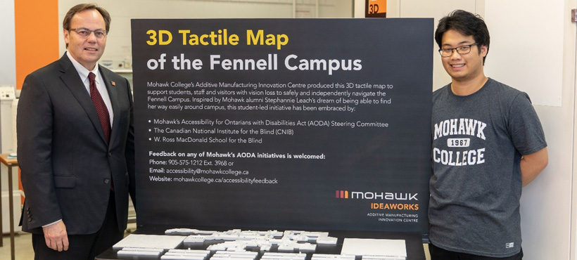 Mohawk president Ron Mckerlie posing with student in front of 3d tactile map sign
