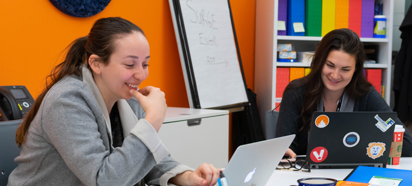 Two students looking at their laptop and smiling