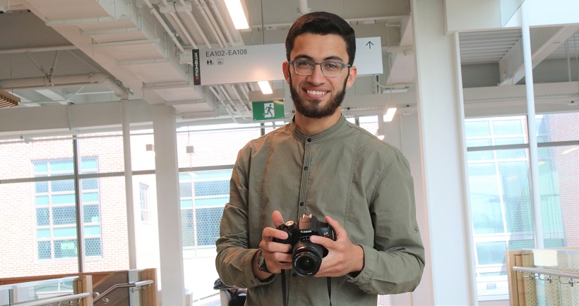 Student standing while holding a camera