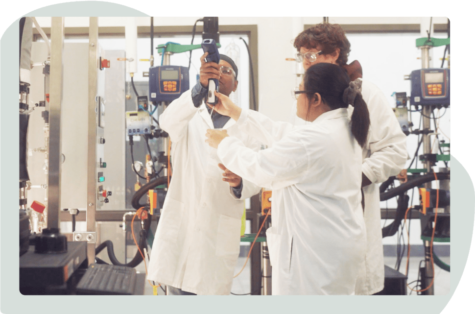 Three students in lab coats working together in a lab
