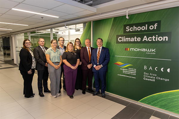Group image with the President in front of the School of Climate Action wall banner.