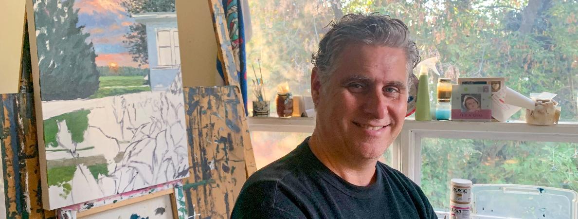 James Gummerson stands in his studio amongst various canvases, surrounded by artworks both completed and in progress.