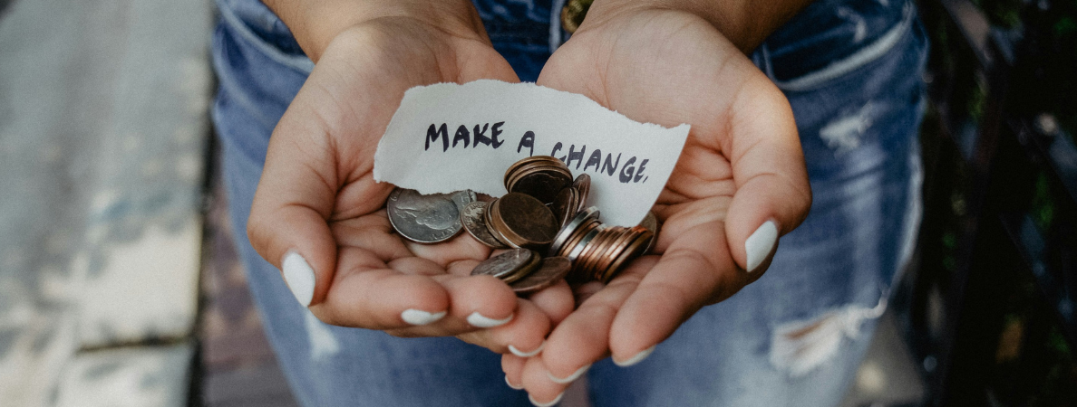 A pair of hands holding some coins and a slip of paper that says "Make A Change"