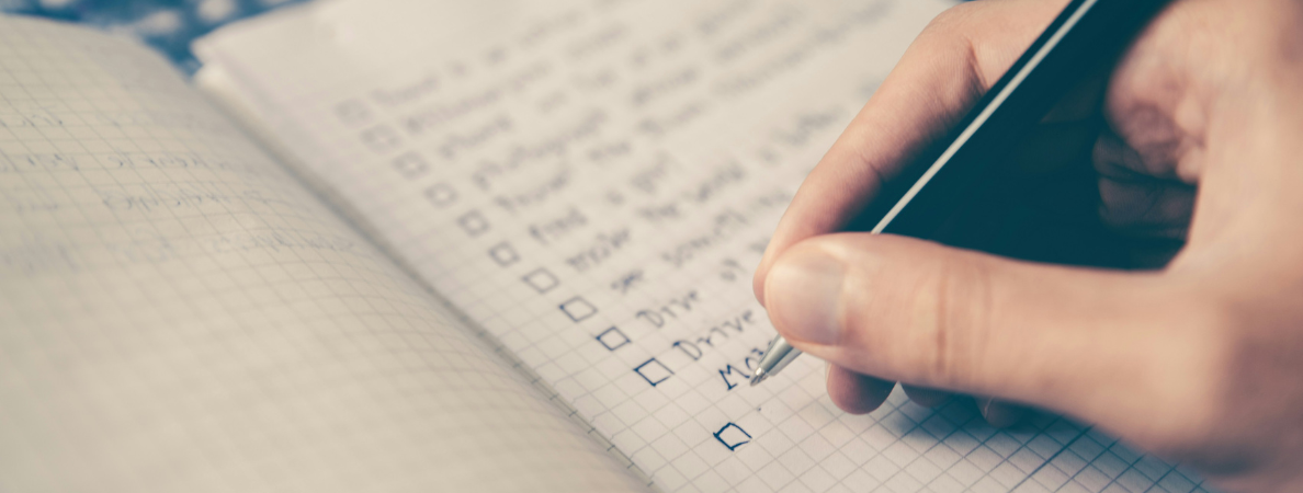 An image of a notebook with a checklist written in it and a hand with a pen about to check off one of the tasks