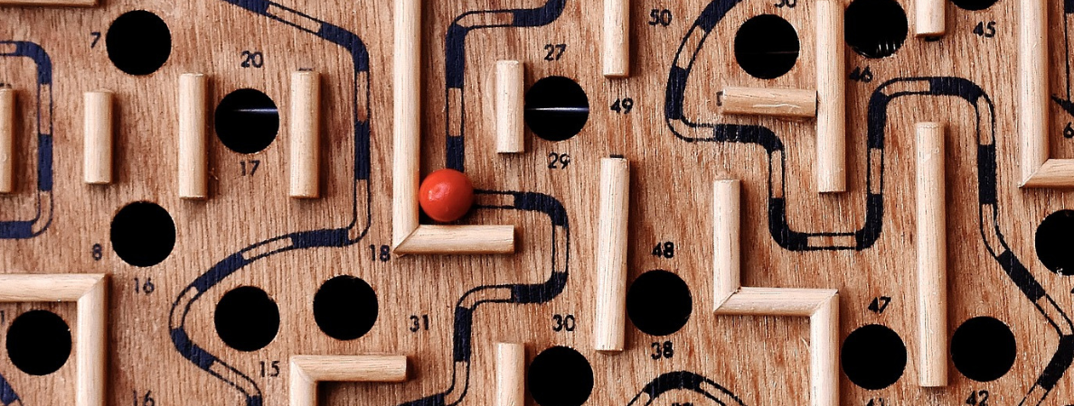 An image of a wooden maze puzzle with a red ball tucked in one of the corners