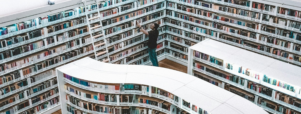 An image of a large library with a man looking at a book.