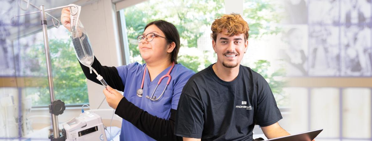 A student holding IV vitals and the other student on a laptop.