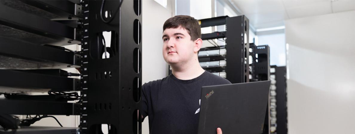 Garret Smink holding a computer while looking at a computer server tower.