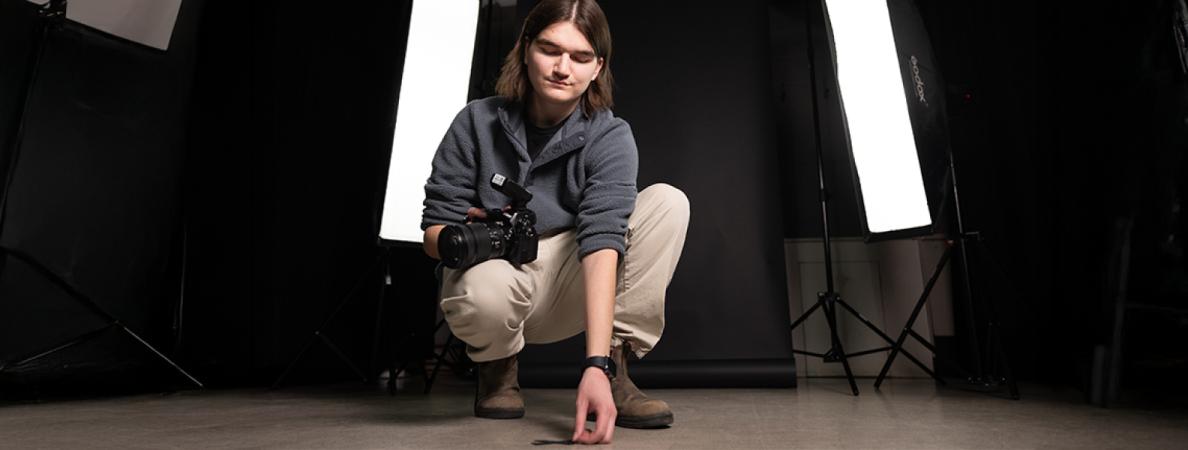 Logan crouching holding a camera.