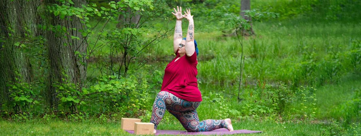 Woman pose on yoga mat with hands in air and one knee on ground