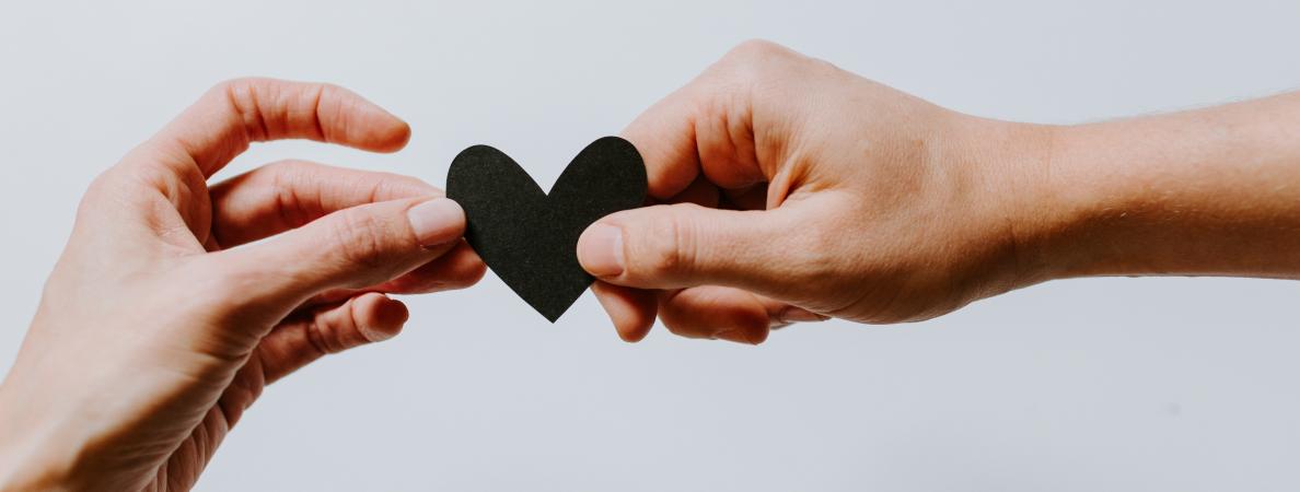 two hands holding a black paper heart