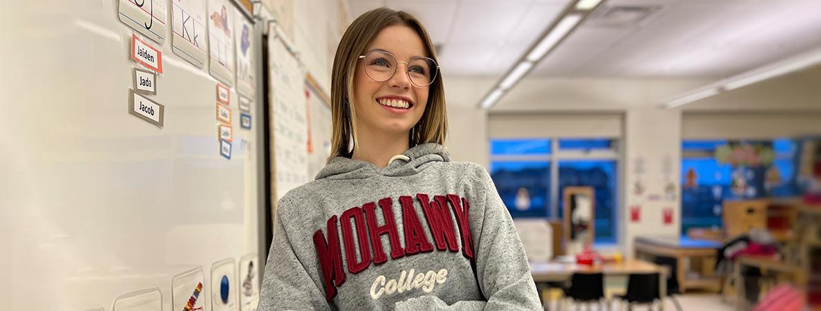 Jessica standing in a kindergarten classroom wearing a Mohawk College hoodie