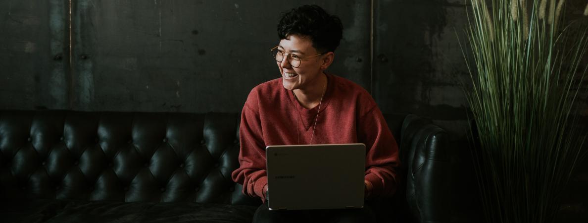 woman wearing glasses sitting on couch with laptop open, smiling