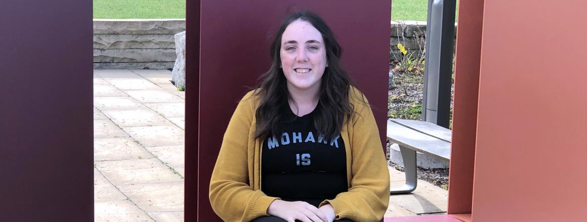 Photo of Jenna sitting by Mohawk sign
