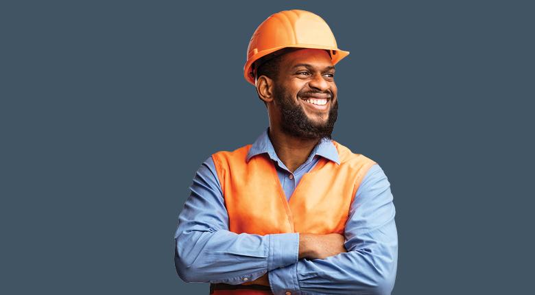 "An employer in a construction site wearing an orange waistcoat and helmet."