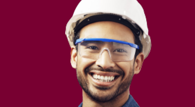 An image of a young man wearing a hardhat, safety glasses and a safety vest smiling