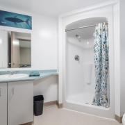 a white washroom with a sink, mirror above the sink, shower, and blue shower curtain.