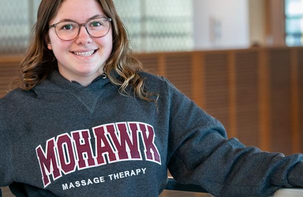 Serena smiles as she stands against a balcony railing overlooking the atrium in the EA wing at Mohawk College.