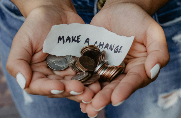 A pair of hands holding some coins and a slip of paper that says "Make A Change"