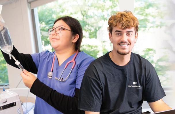 A student holding IV vitals and the other student on a laptop.