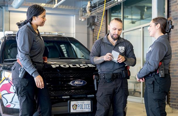 Three Mohawk Advanced Police Studies students in front of a police car talking.
