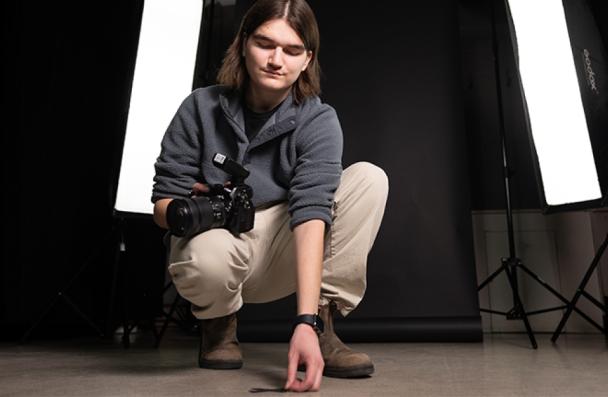 Logan crouching holding a camera.