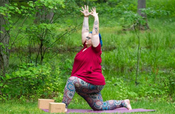 Woman pose on yoga mat with hands in air and one knee on ground