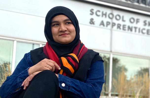 Maskan sitting in front of Stoney Creek Campus for Skilled Trades and Apprenticeship