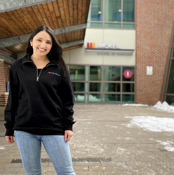 Luz in a Mohawk sweater standing in front of the McKeil School of Business