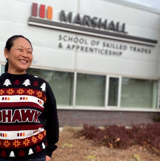 Michelle standing in front of the Marshall School of Skilled Trades & Apprenticeship building in a holiday sweater