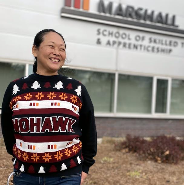 Michelle standing in front of the Marshall School of Skilled Trades & Apprenticeship building in a holiday sweater